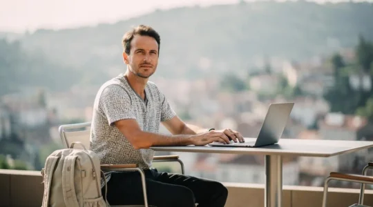 Un travailleur nomade installé sur une terrasse ensoleillée, ordinateur portable ouvert, incarnant l'équilibre entre liberté de voyage et sérénité professionnelle