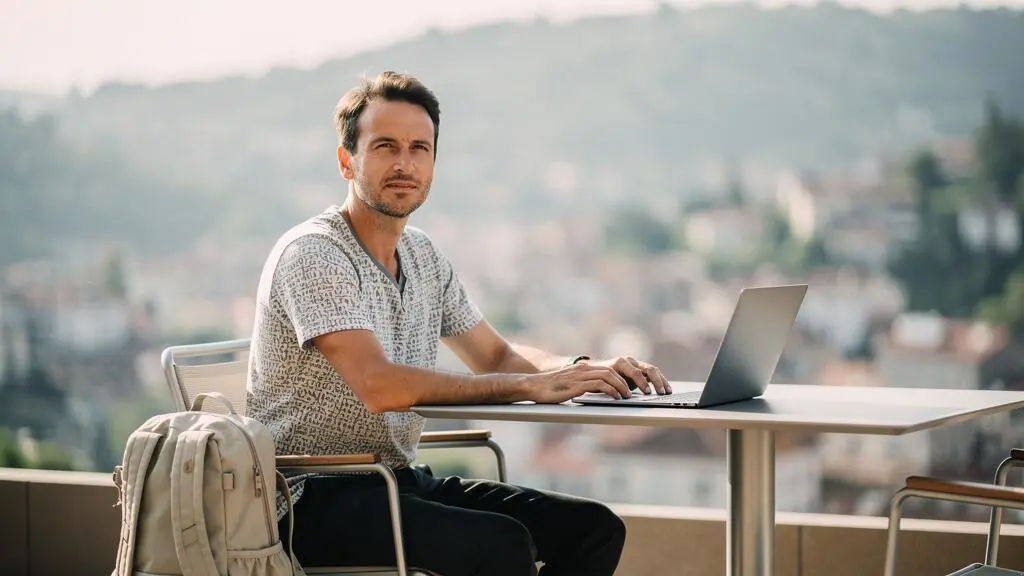 Un travailleur nomade installé sur une terrasse ensoleillée, ordinateur portable ouvert, incarnant l'équilibre entre liberté de voyage et sérénité professionnelle